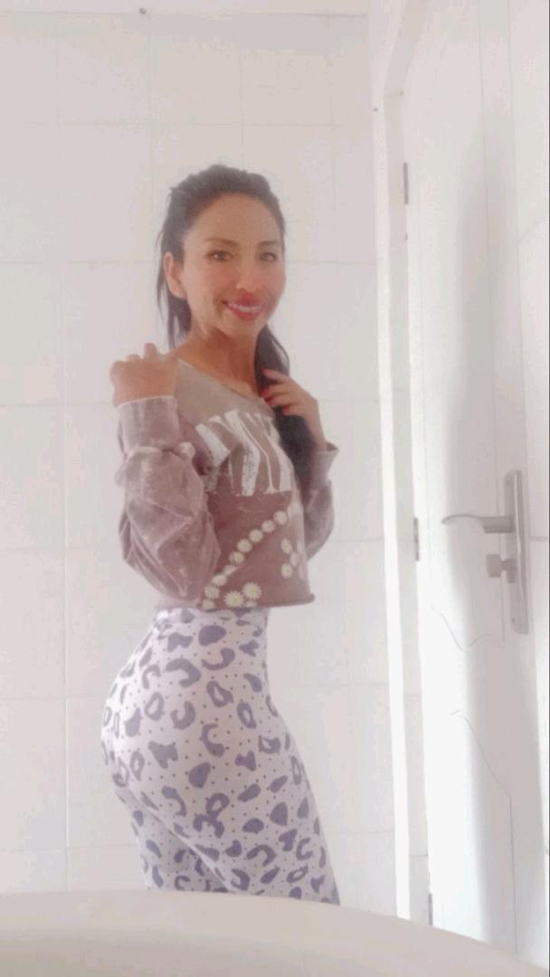 A girl from Bolivia standing by a bright wall, phone in hand